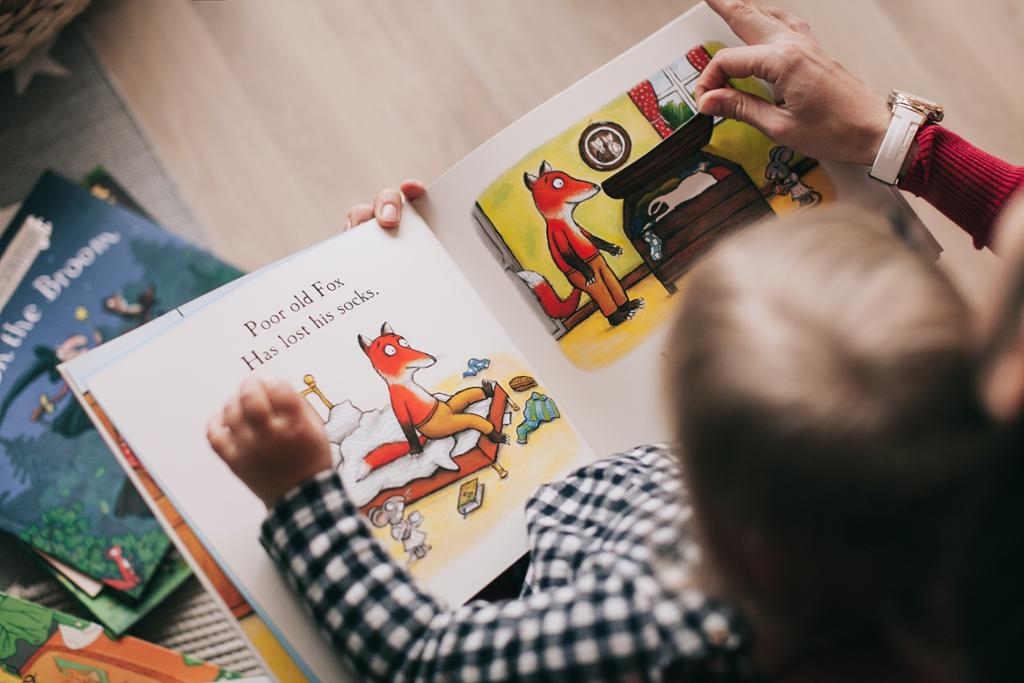 Et barn leser i en bildebok sammen med en voksen. Foto.