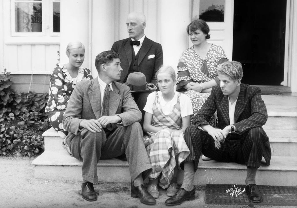 Portrett av Knut Hamsun med familie. De sitter på en utetrapp i pentøy fra 1930-tallet. Foto.