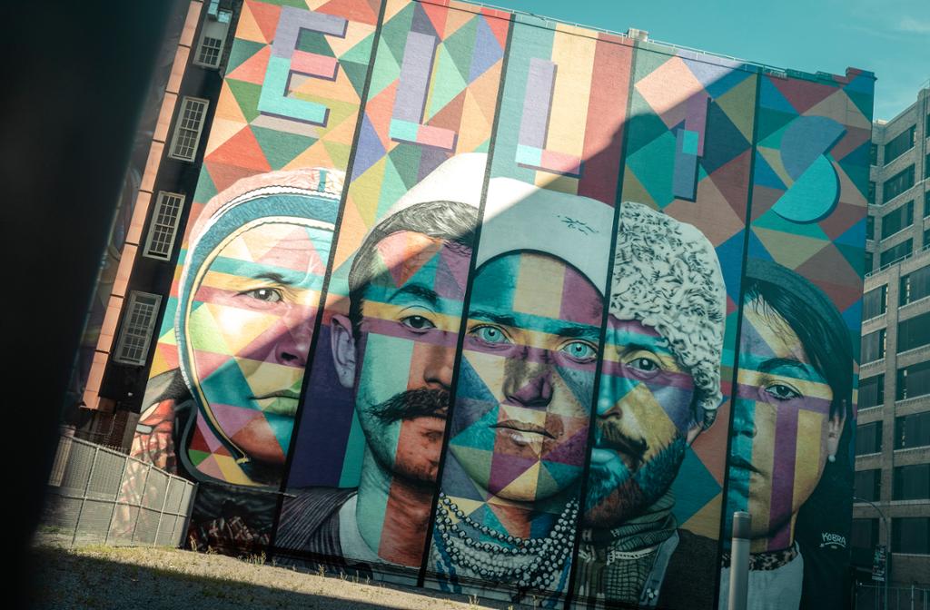 Large mural by the artist Eduardo Kobra. It features different faces and the text ‘Ellis’ is painted over a five-story building in New York. Photo.