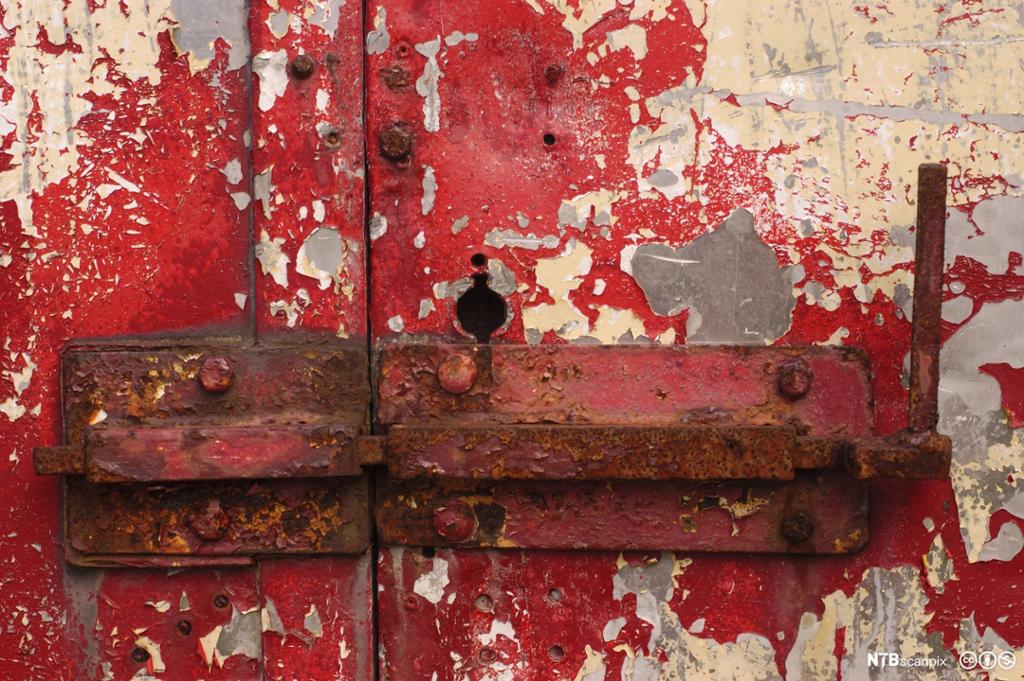 Rusten lås på dør med avflasset rødmaling. Foto.
