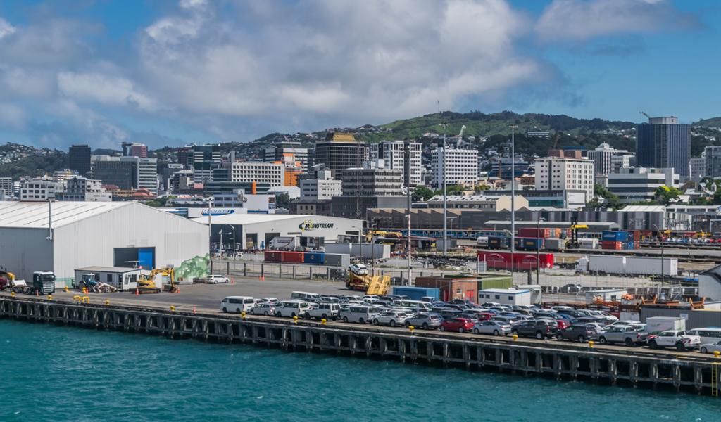 Photo: We see a harbour with high-rise buildings in the background. There are many cars parked on the harbour. One of the buildings in the harbour has a sign that reads 'Mainstream'. 