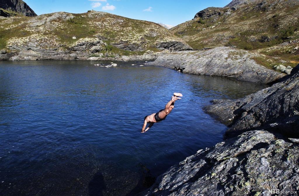 En person stuper ut i et fjellvann. Foto.