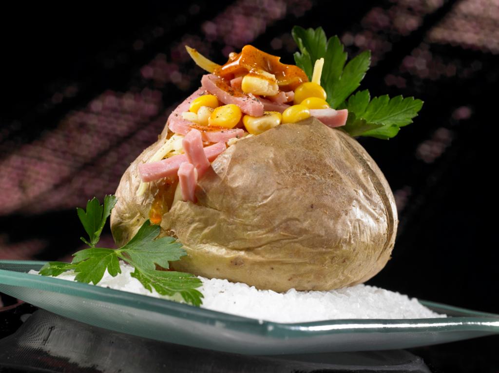 En stor, bakt potet fylt med skinke, mais og ost, pyntet med persilleblader. Foto.