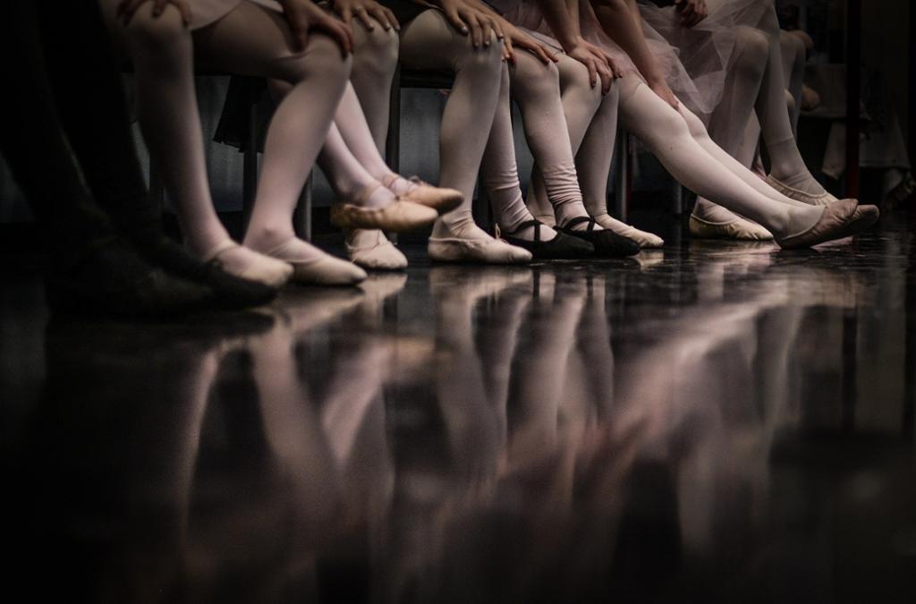 Kne og føtter til ballettdansere speiler seg i blank gulvflate.foto.