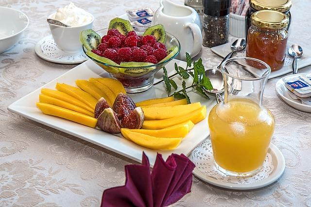 Dekt bord med bær i ei skål, mango og gul drikke i ein karaffel. Foto.