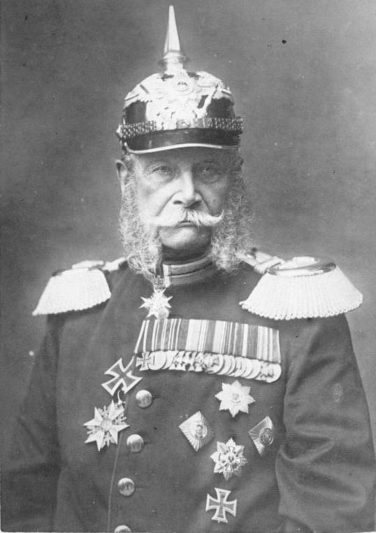 Portrett av den første tyske keiseren, Vilhelm 1. Han har uniform med en mengde medaljer og utmerkelser, prangende epåletter  og hjelm med en høy metallpigg på toppen. Foto. 