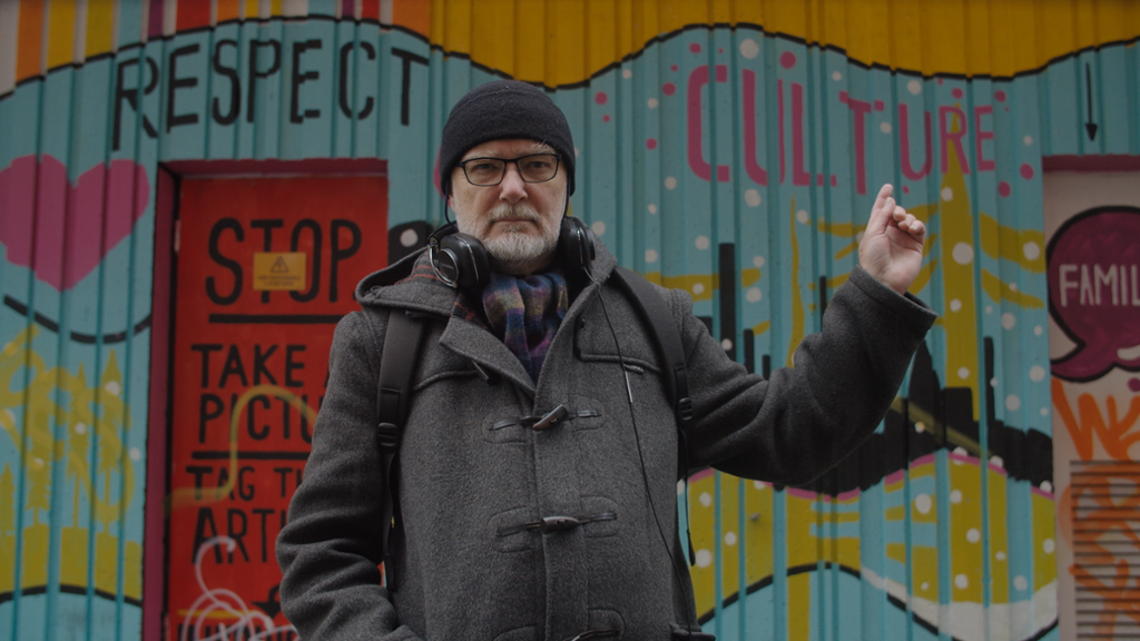 Forskar Viggo Vestel står foran ein vegg med gatekunst og peiker på ordet "culture". Foto. 