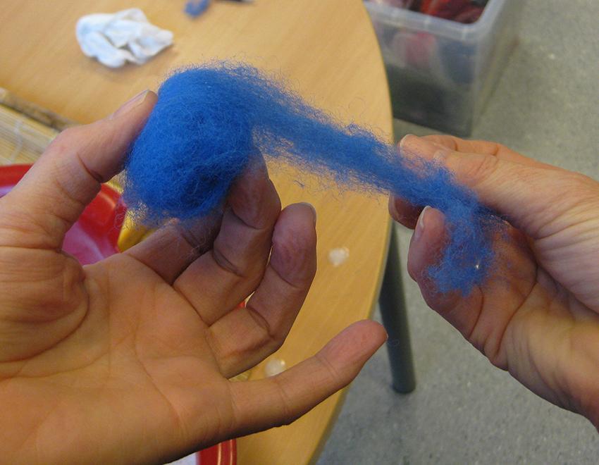 En person ruller sammen blå ull til en ball. Foto.