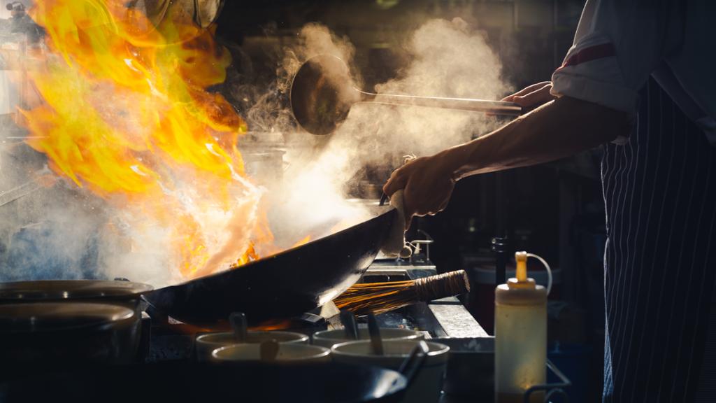 En kokk flamberer mat i ei wokpanne. Foto.