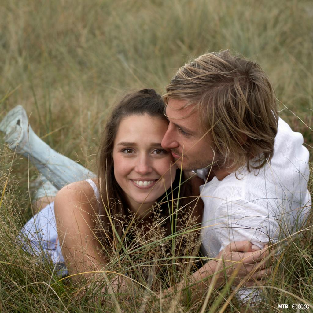 Et ungt forelsket par ligger i gresset. Foto.