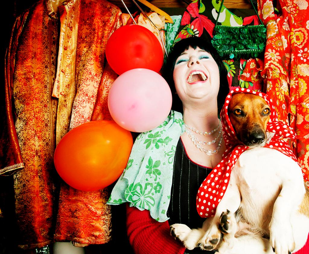 Portrett av fargerike Christine Khot med ballonger og en utkledd hund. Foto.