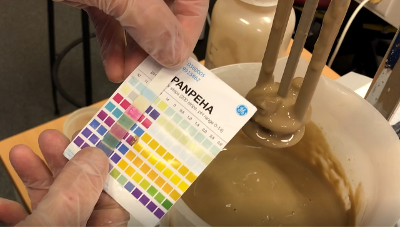Hender med engangshansker holder pH-papir og måler pH-verdien i borevæske. Foto.