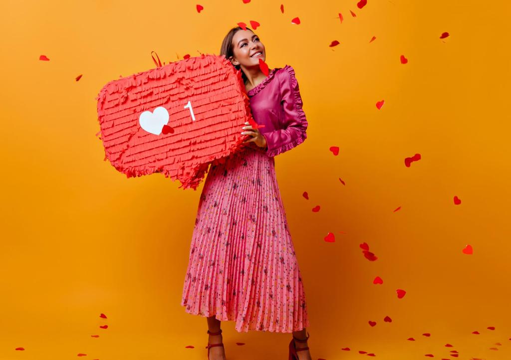 Jente med rosa kjole og hjerter som faller ned over henne. Hun holder en stor, rød snakkeboble med et hjerte på. Foto.