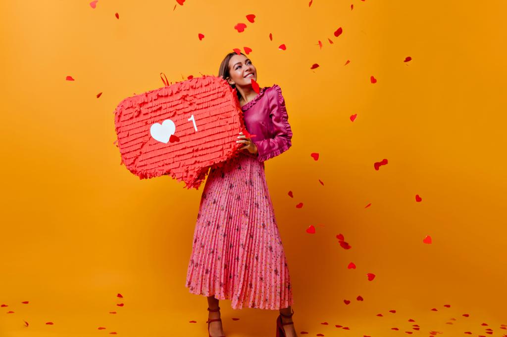 Jente med rosa kjole og hjerter som faller ned over henne. Hun holder en stor rød snakkeboble med et hjerte og et ett-tall på. Foto.