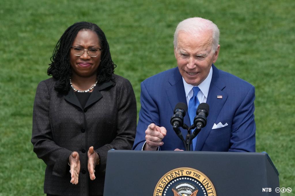 Photo: Supreme Court justice Ketanji Brown Jackson and President Joe Biden stand on a lawn. In front of them is a lectern with microphones. The lectern has the seal of the president. 