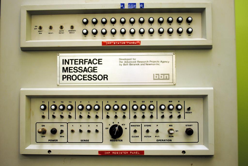 Frontpanel med mange knapper og gammeldagse brytere merket med et skilt der det står "Interface Message Processor". Foto.