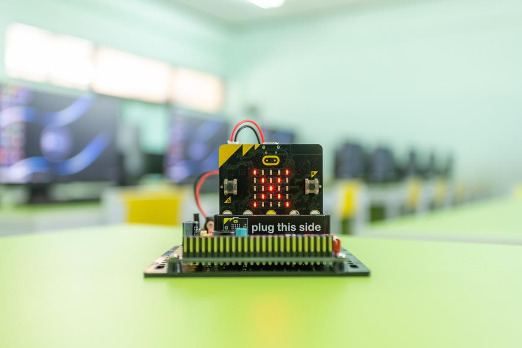 En micro:bit som er kopla til et koplingsbrett. Den er strømsatt, og i LED-matrisen vises bokstaven X. Foto.