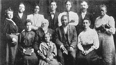 Gammelt, slitt gruppebilde i svart-hvitt med en blanding av både svarte og hvite, kvinner og menn. Foto.