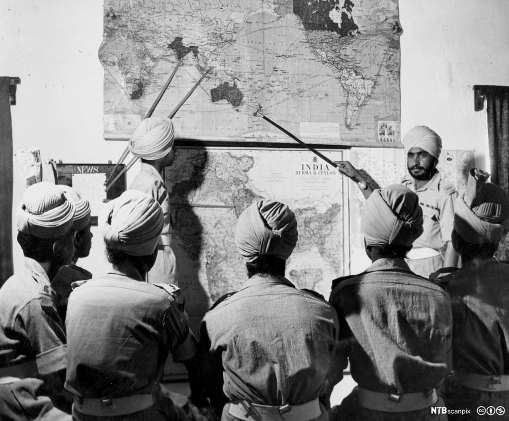 Menn med turban peikar på land på eit verdskart. Fotografi.