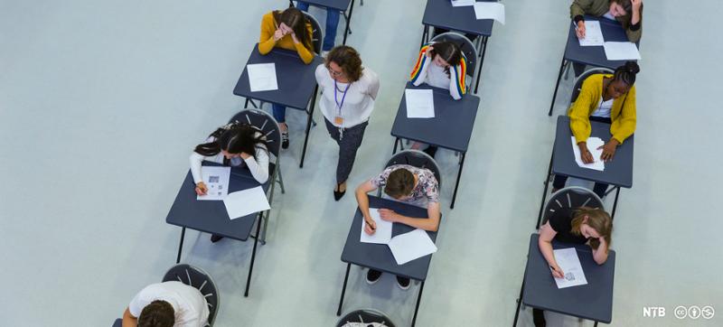 Elever sitter ved pulter i eksamenslokale, svarer på skriftlig oppgave. Foto