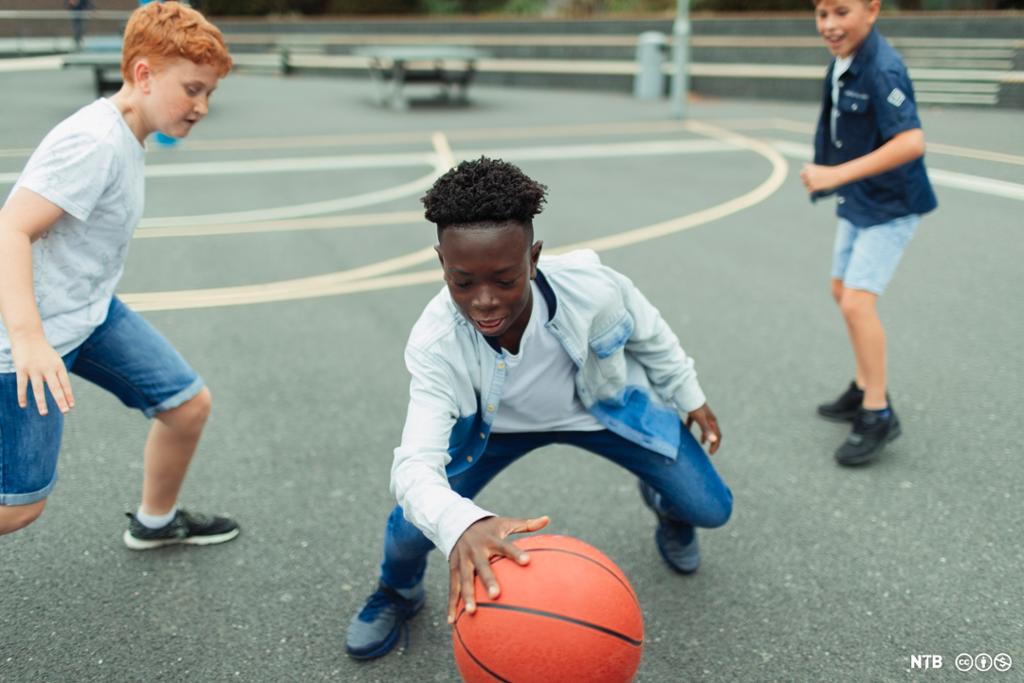 Tre gutter spiller basket i skolegården. Foto.