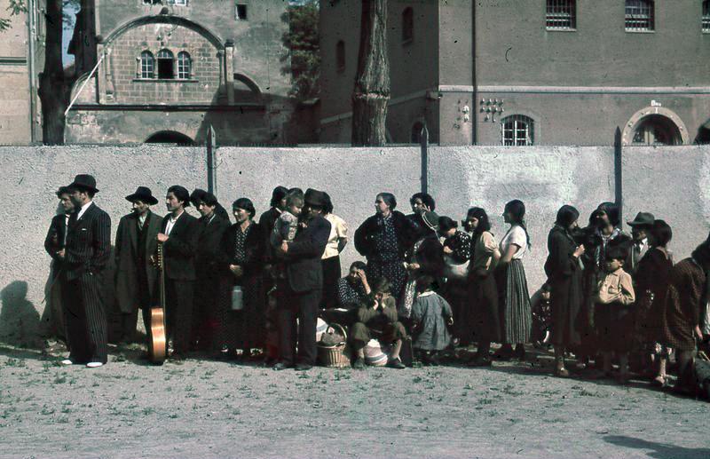 Mange voksne og barn med ulik bagasje står foran en mur. Foto. 