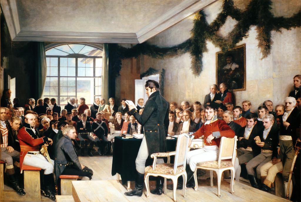 Riksforsamlingen på Eidsvoll 1814.En gruppe menn sitter langs veggen og hører på en som taler. Maleri.