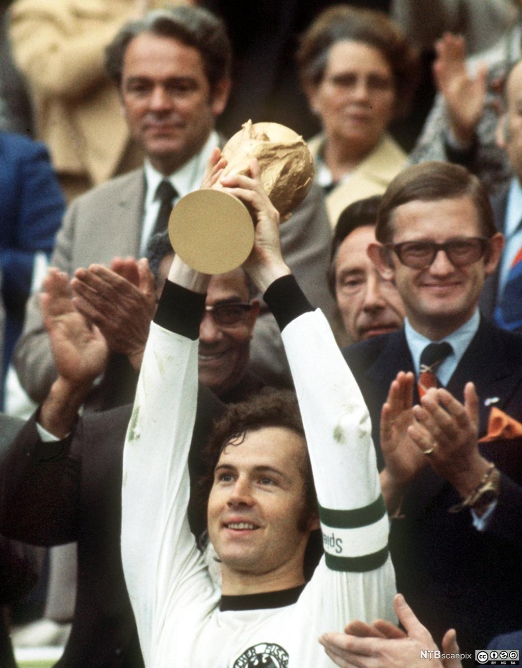 Franz Beckenbauer, tidligere kaptein på det tyske landslaget i fotball, løfter VM-pokalen. Foto.