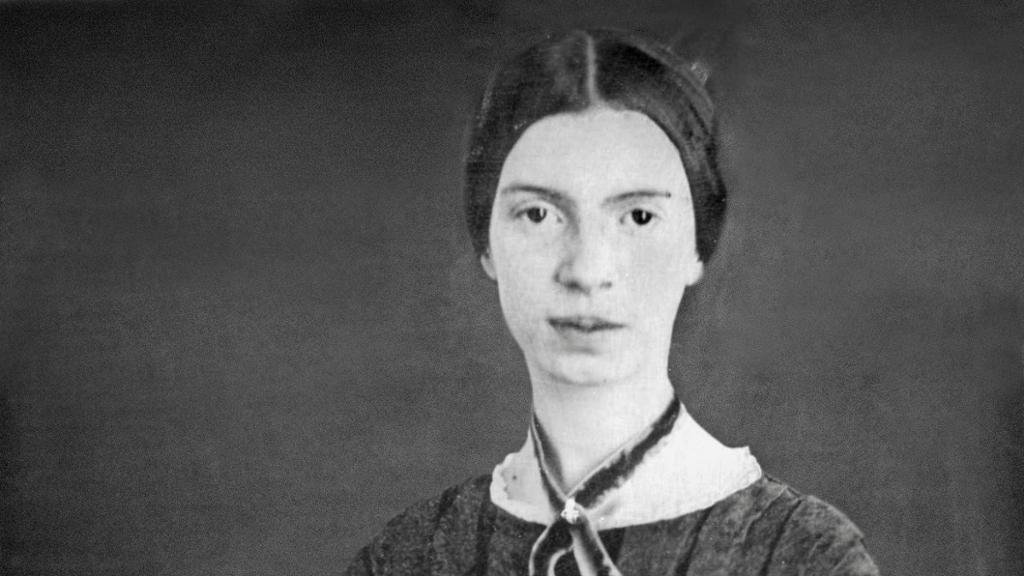 Photo: Portrait of Emily Dickinson. We see a woman with large brown eyes and dark hair. She has a ribbon tied around her neck. 