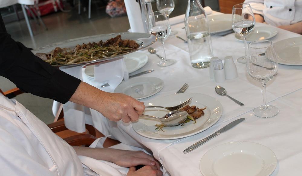 Servitør legg mat på tallerkenen til ein gjest. Foto.