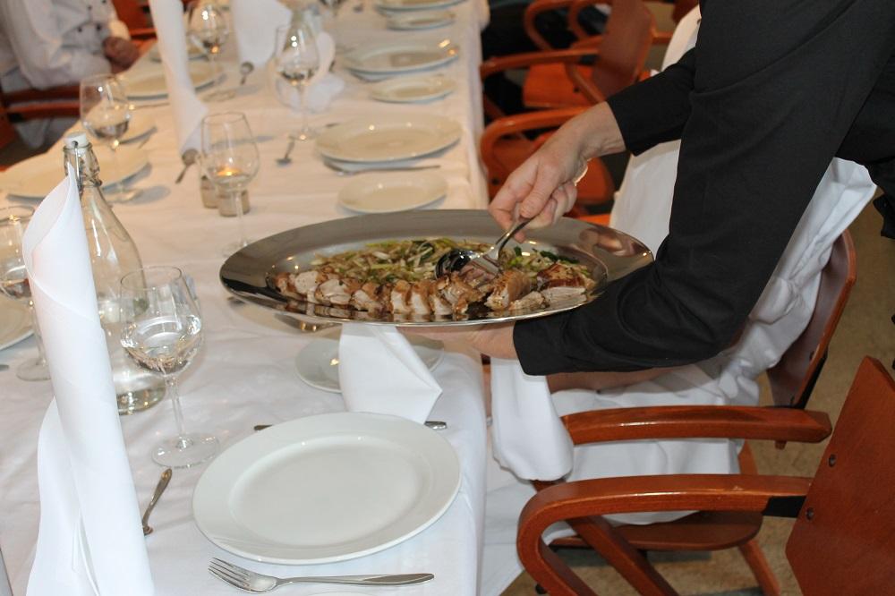 Servitør serverer mat fra et stort fat. Foto.