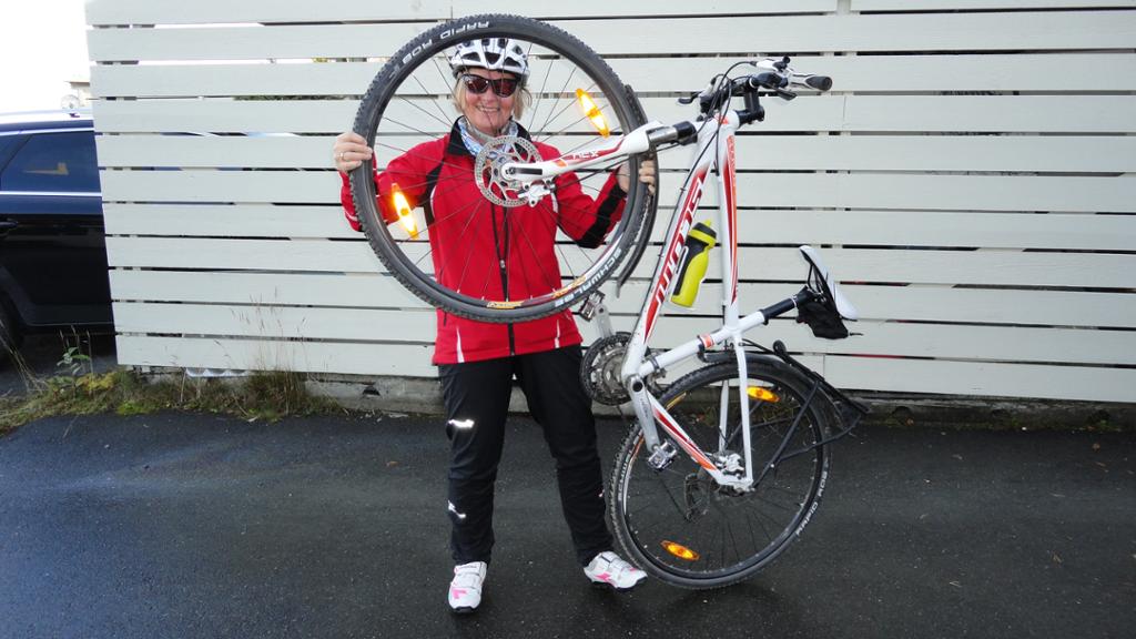 Kvinne holder opp en sykkel og ser gjennom forhjulet. Foto.