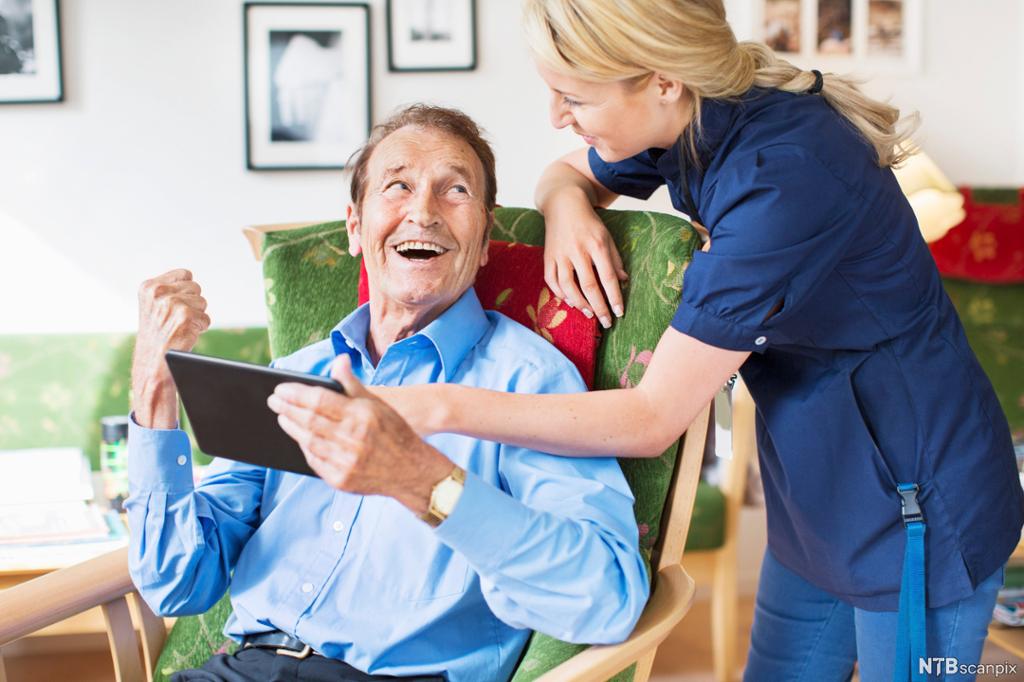 Eldre mann og helsefagarbeider kommuniserer om bruk av nettbrett. Foto.