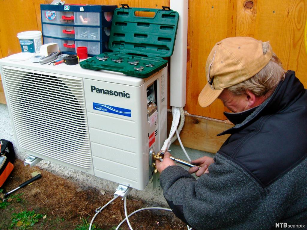 En mann installerer en varmepumpe. Foto.