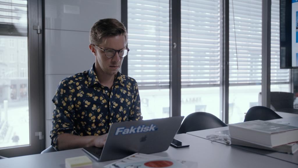En mann i trettiåra sitter ved et bord og jobber på en datamaksin. Foto.
