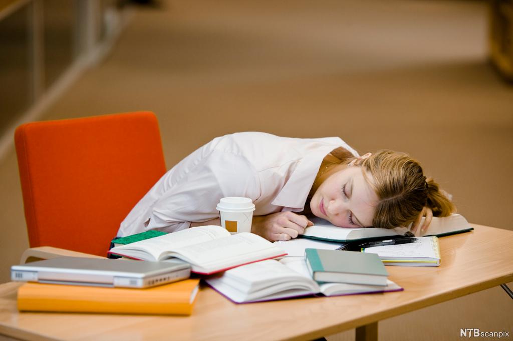 Ung kvinne sover med hodet på åpne bøker. Foto.