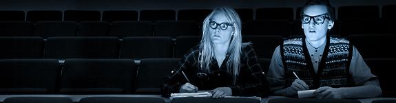 En ung kvinne og en ung mann sitter i en kinosal og noterer i et skrivehefte. Foto.