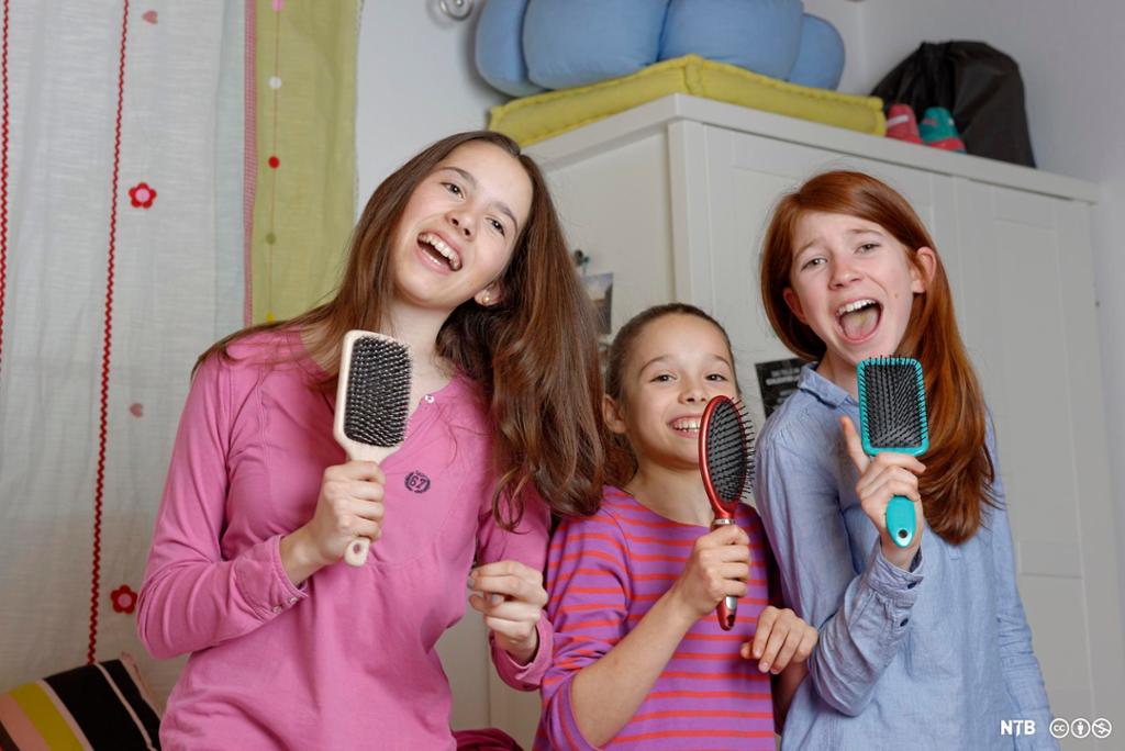 Tre jenter som står og synger og bruker hårbørster som mikrofon. Foto.