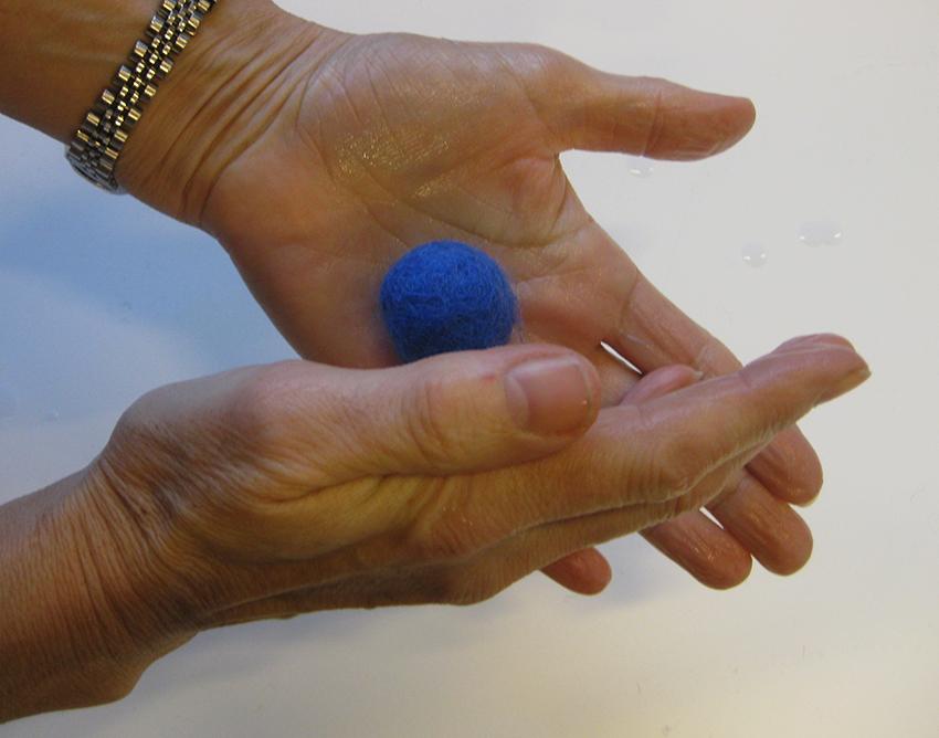 En person triller ei blå ullkule mellom hendene. Foto.