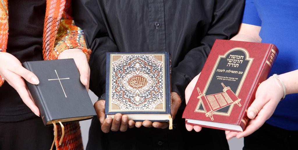 Tre personer holder fram hver sin bok. Boka til venstre har et kors på omslaget. Boka i midten har arabisk skrift og utsmykning. Boka til høyre har hebraisk skrift med bilde av en skriftrull. Foto.