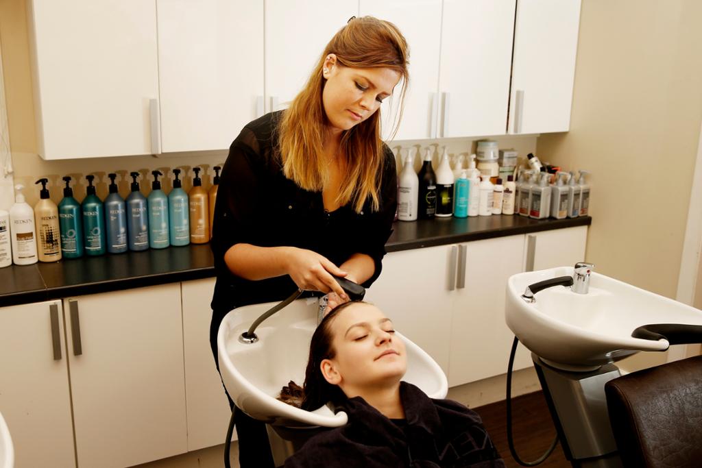 Frisør skyller håret til kvinnelig kunde i frisørsalong. Foto.