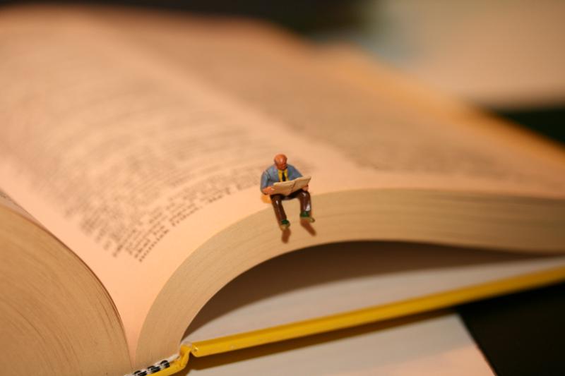 Miniature of a man reading is placed on the edge of a book. Photo. 