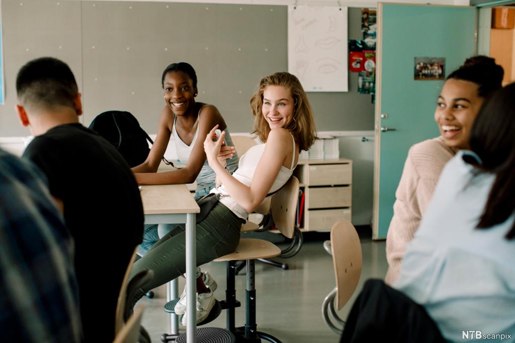 Jenter ler ertende mot en gutt i et klasserom. Foto. 