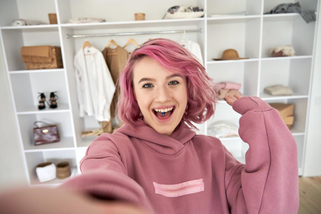 Jente med rosa hår og rosa genser spiller inn en film med seg selv i. Foto. 