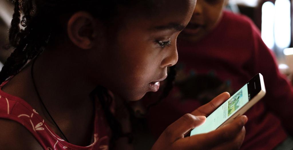 Afrikansk barn les på mobil. Foto.
