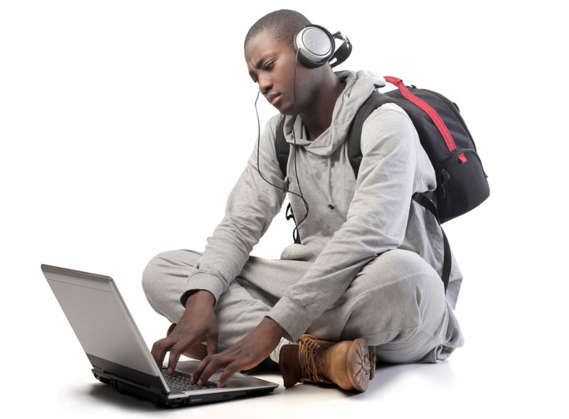 Farga gutt skriver på laptop med ryggsekk og hodetelefoner. Foto.