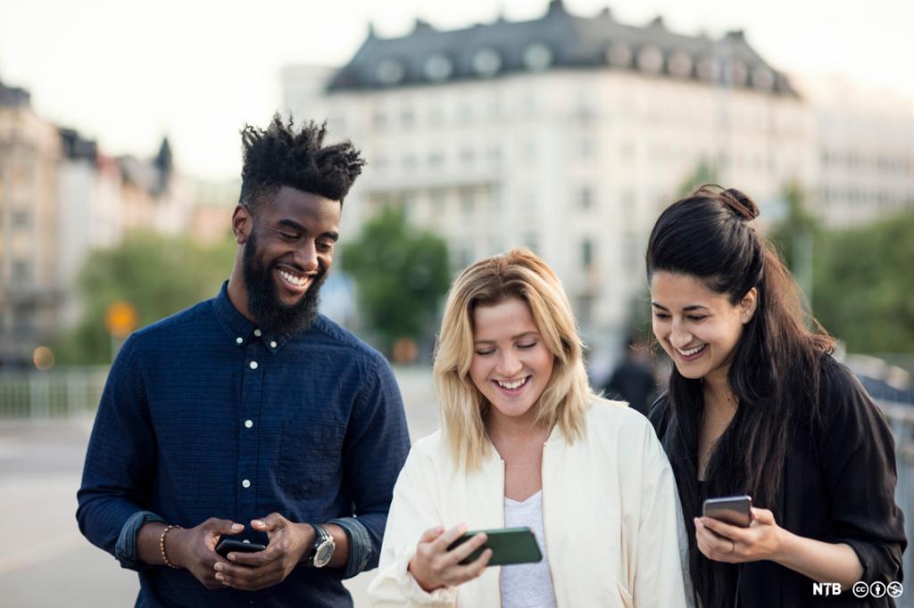 Tre unge med ulik etnisitet ser på en smarttelefon. Foto.