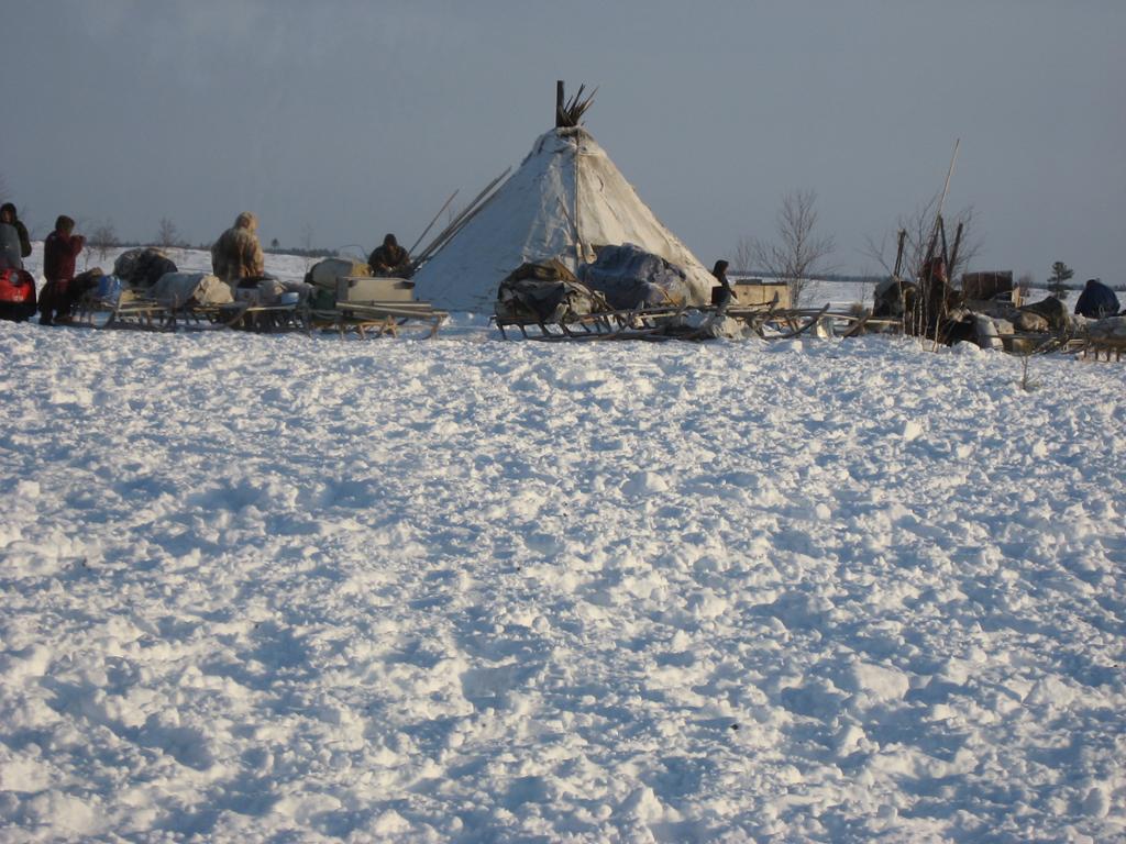 Byggverk med teltvegger på snødekt mark, med folk og sledar rundt. Foto.
