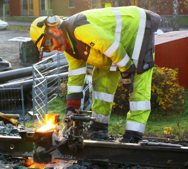 Banemontør med verneutstyr og arbeidsklede heilsveisar jernbaneskjener. Foto.