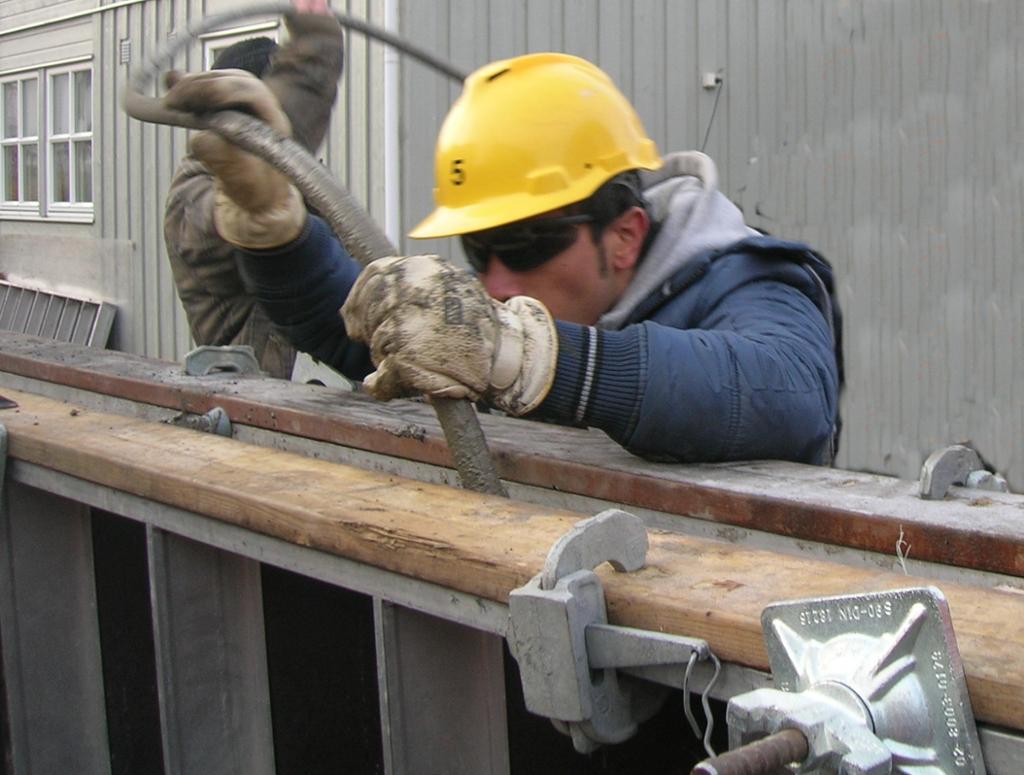 Betongarbeider med vernebriller, hjelm og hansker ved støping av betong. Foto.